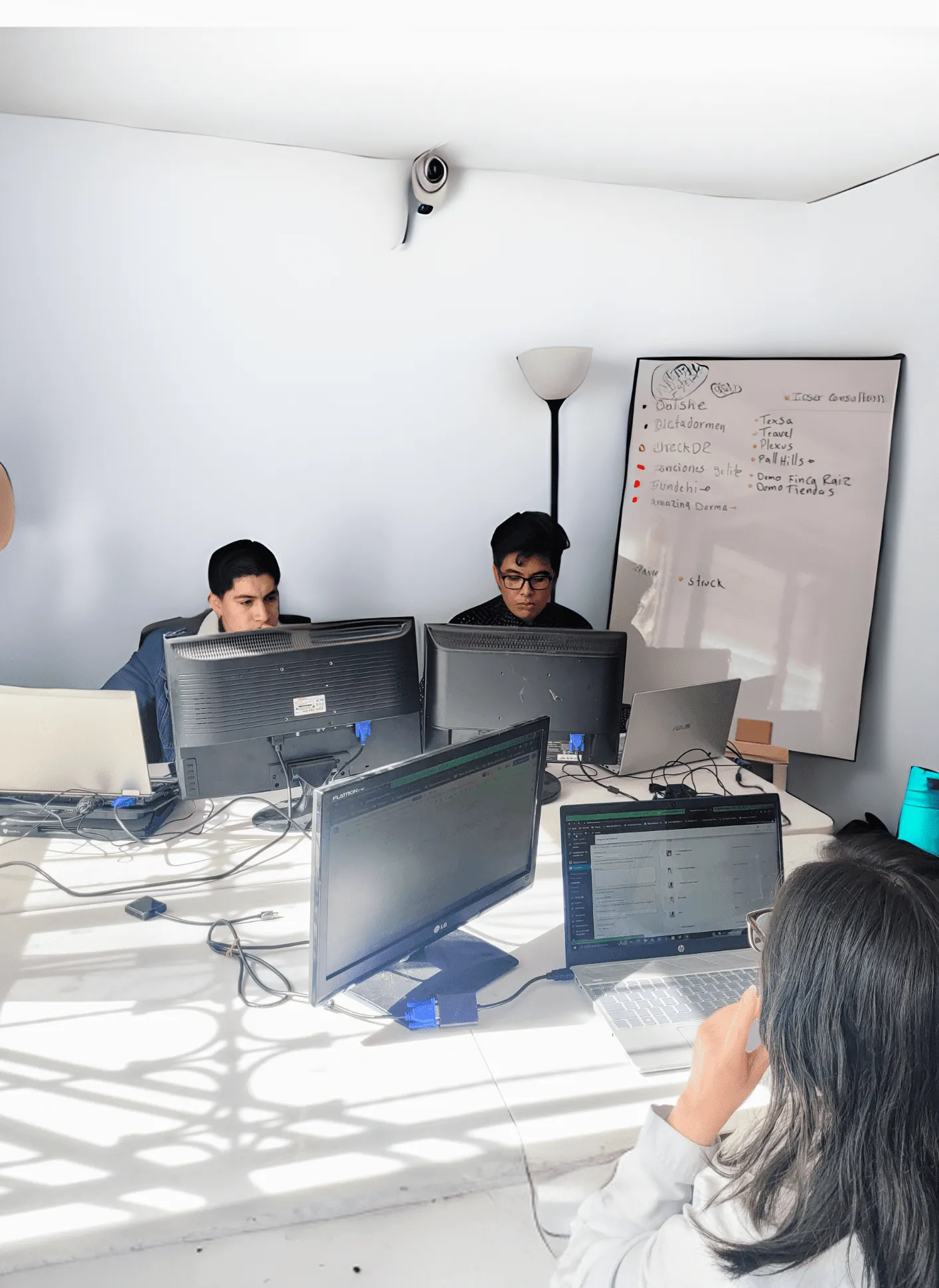 Tres integrantes del equipo de MTechnology trabajando en sus escritorios, con el tablero de proyectos en curso al fondo