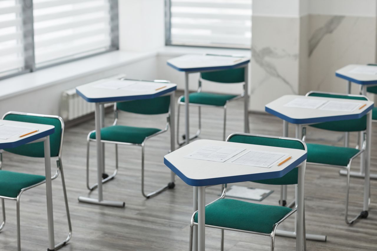 Pupitres con hojas de examen listos en un aula vacía, imagen de la preparación de una jornada de evaluaciones