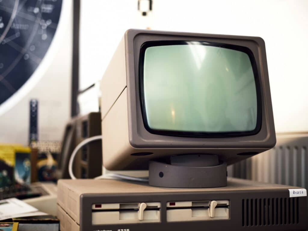 Computador antiguo de carcasa beige con monitor de fósforo verde y dos unidades de disquete, símbolo del software heredado