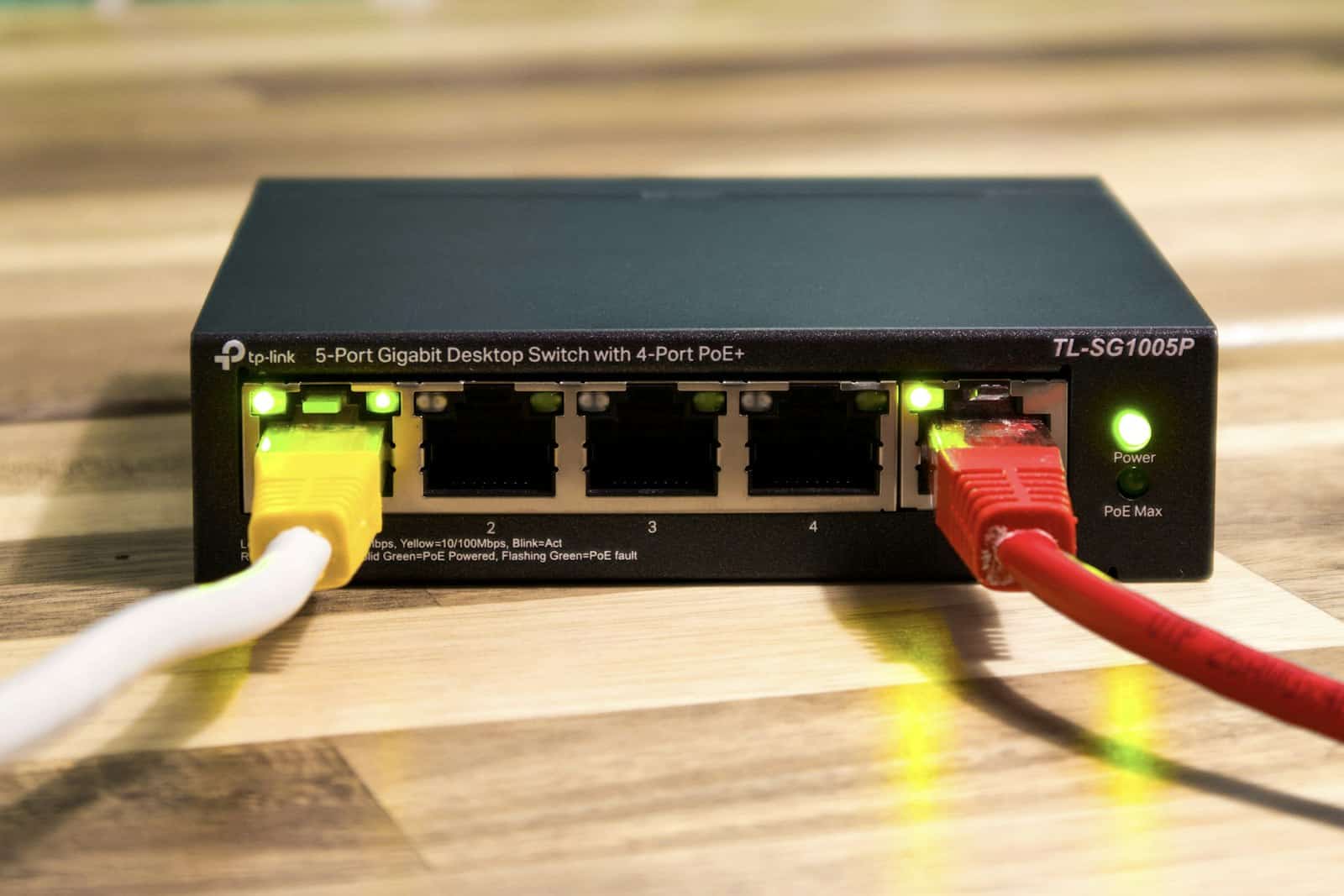 Switch de red de cinco puertos con cables Ethernet amarillo y rojo conectados y luces verdes encendidas, metáfora de la conexión entre sistemas
