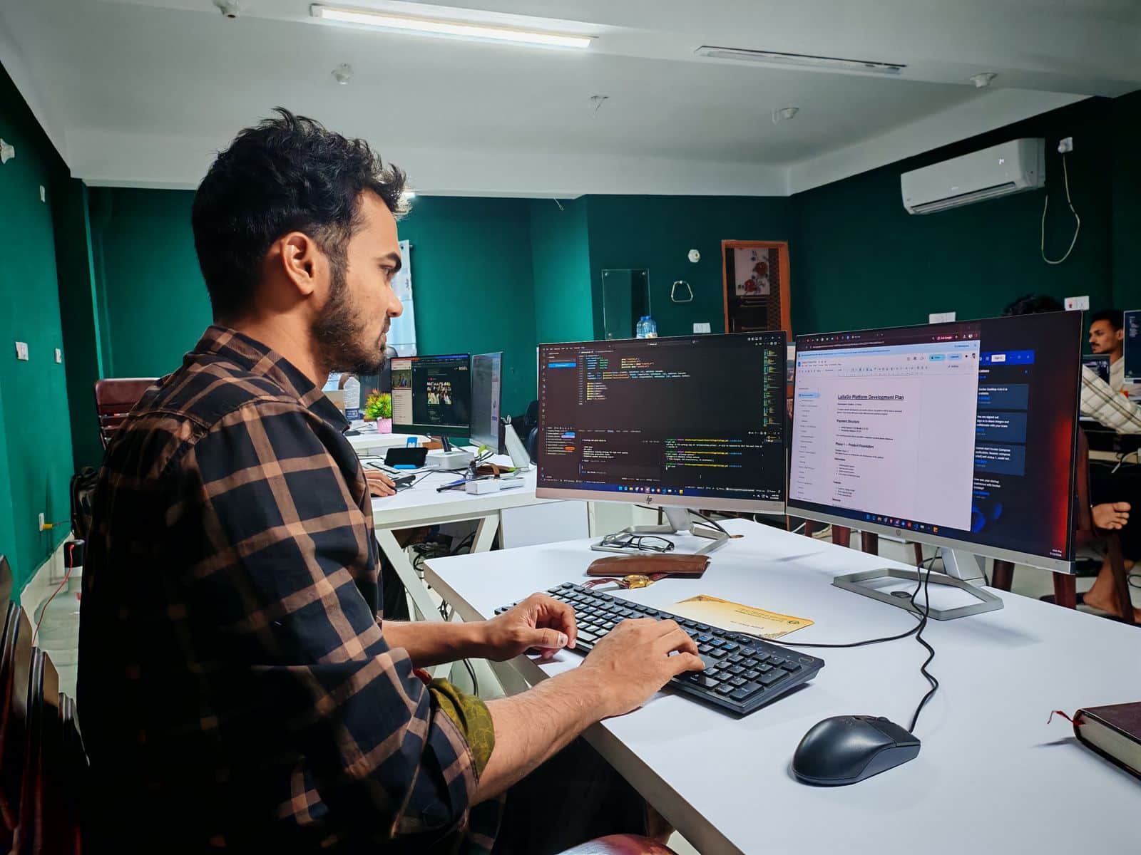 Desarrolladora de software trabajando con código en dos monitores en una oficina luminosa
