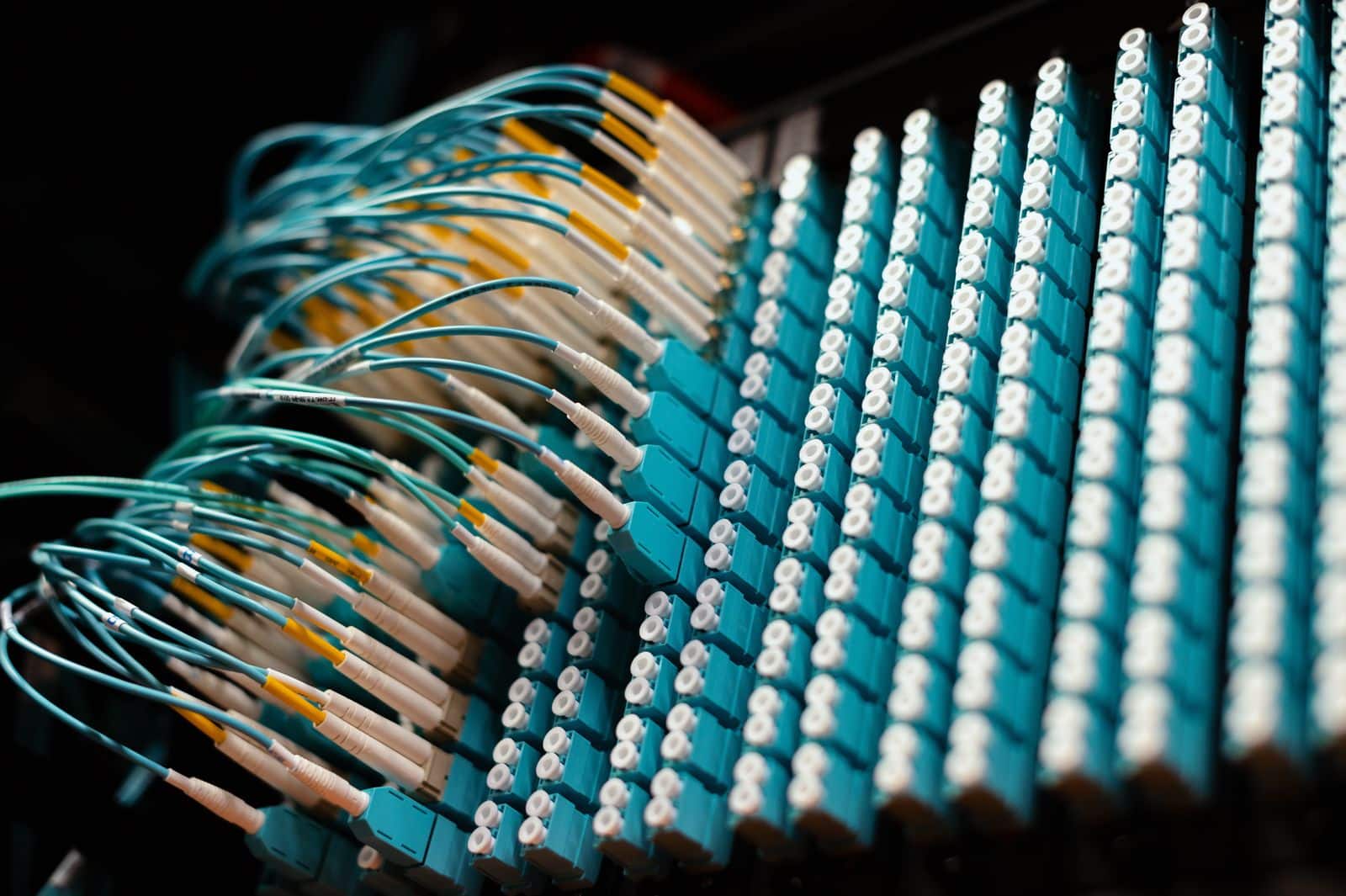 Cables de fibra óptica azul turquesa conectados en un panel de conexiones, imagen que ilustra sistemas conectados entre sí