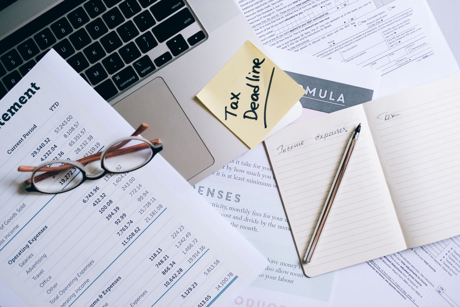 Escritorio con una laptop, estados financieros impresos, gafas y un cuaderno de ingresos y gastos