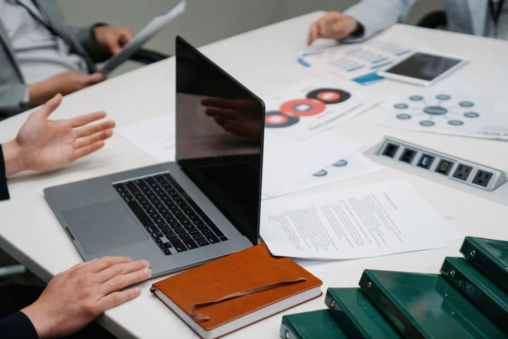 Mesa de reunión con una laptop y documentos mientras un equipo compara opciones de software
